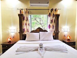 A hotel room with a bed, floral curtains, bedside lamps, and a view of greenery outside. - Yoga Dreams Negril (Negril)