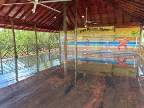 A covered area with a wooden floor and ceiling, a sign reading "yoga Dreams Negric", and a mural of yoga poses. - Yoga Dreams Negril (Negril)