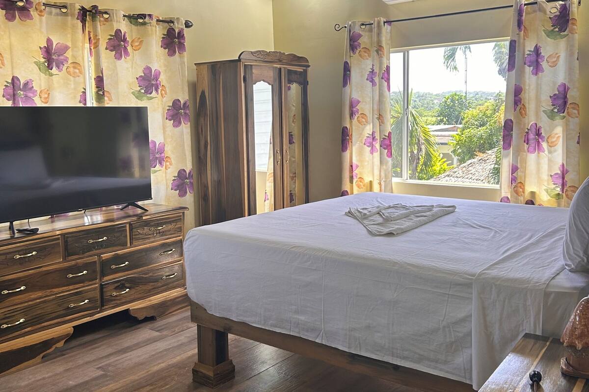 A bedroom with a bed, wooden dresser, TV, and an air conditioning unit.