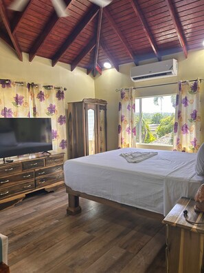A bedroom with a bed, wooden dresser, TV, and an air conditioning unit. - Yoga Dreams Negril (Negril)