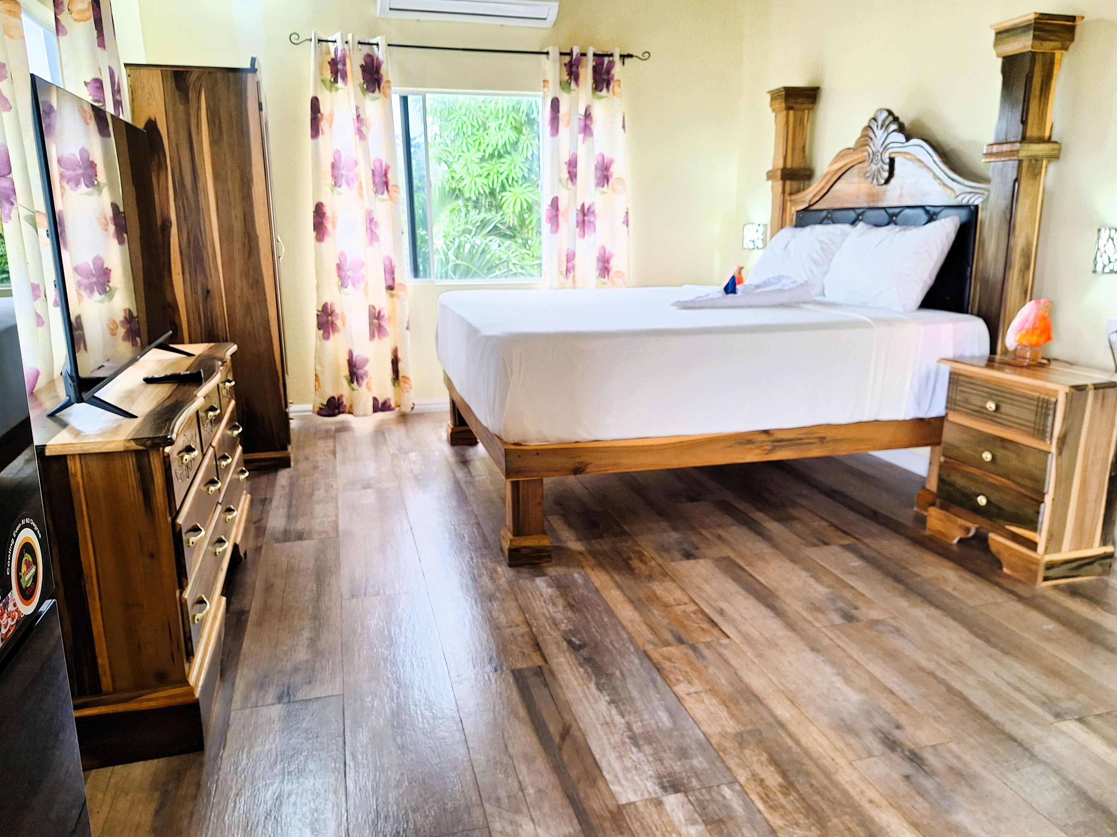 A bedroom with a wooden bed, a dresser, a nightstand, and a TV.