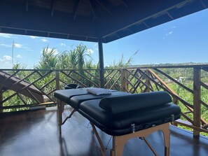 A massage table with a towel on it, set up on a wooden deck with a view of greenery and a clear sky. - Yoga Dreams Negril (Negril)