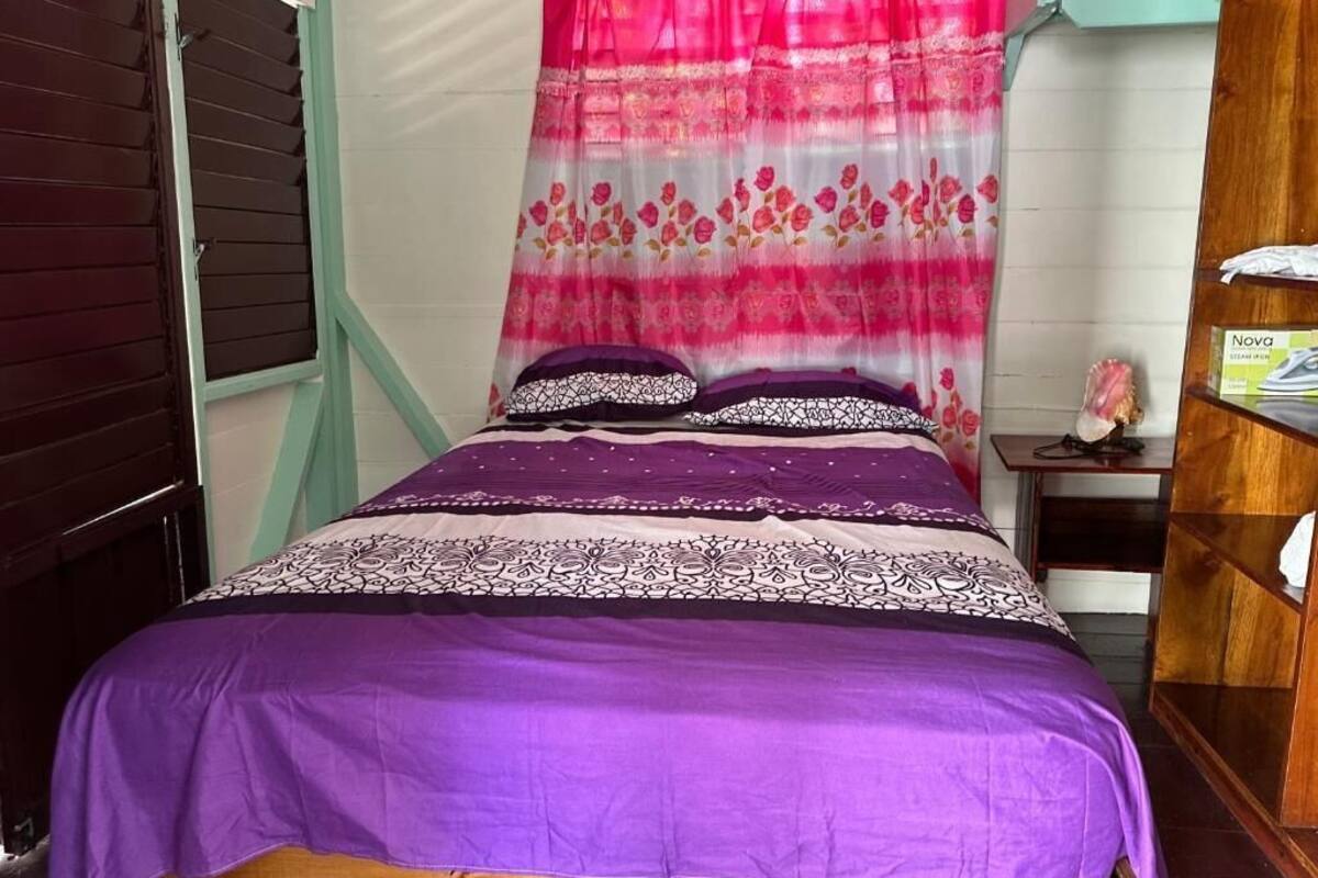 A bed with a purple bedspread and a pink floral curtain.