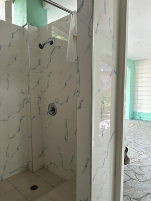 A shower area with marble tiles, a showerhead, and a towel hanging on the wall. - Yoga Dreams Negril (Negril)