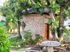 A stone building with a wooden door, surrounded by lush greenery and a mosaic table. - Yoga Dreams Negril (Negril)