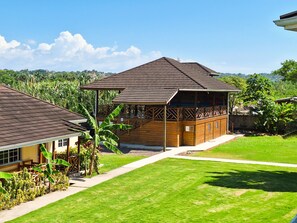 A wooden building with a sloped roof, surrounded by a well-maintained lawn and a backdrop of hills. - Yoga Dreams Negril (Negril)
