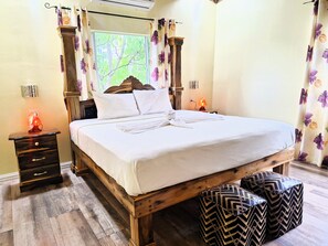 A bedroom with a wooden bed, white bedding, a nightstand with a lamp, and a window with curtains. - Yoga Dreams Negril (Negril)