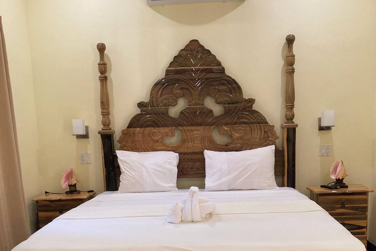 A neatly made bed with a wooden headboard, two bedside tables with lamps, and a wall-mounted air conditioner.