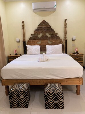 A neatly made bed with a wooden headboard, two bedside tables with lamps, and a wall-mounted air conditioner. - Yoga Dreams Negril (Negril)