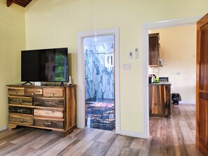 Een kamer met een houten dressoir, een flatscreen televisie en een deur die leidt naar een gang met een gekleurd vloerkleed.