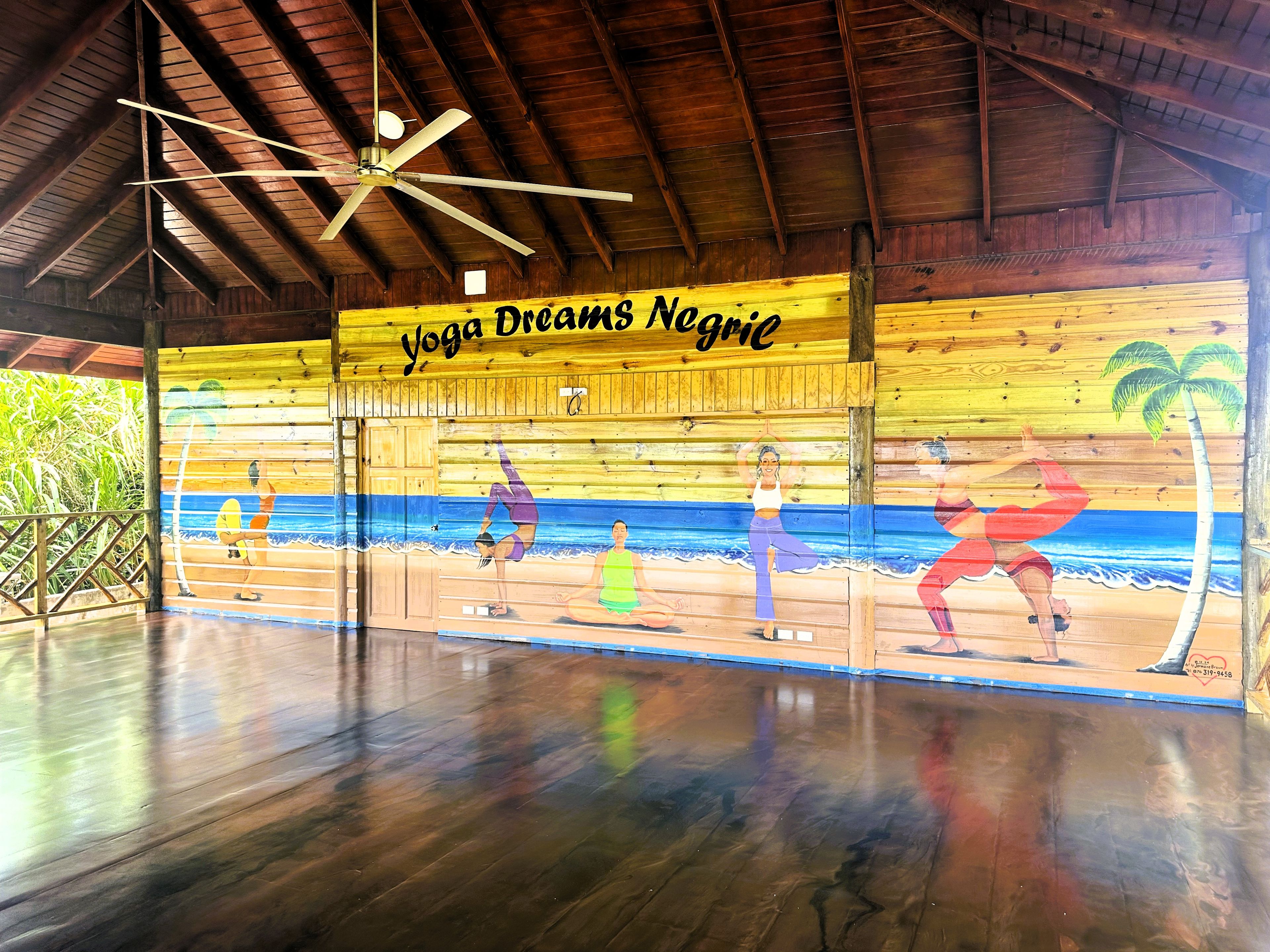 Un studio de yoga doté d’un plafond en bois, d’un ventilateur de plafond et d’une fresque représentant des scènes de plage.