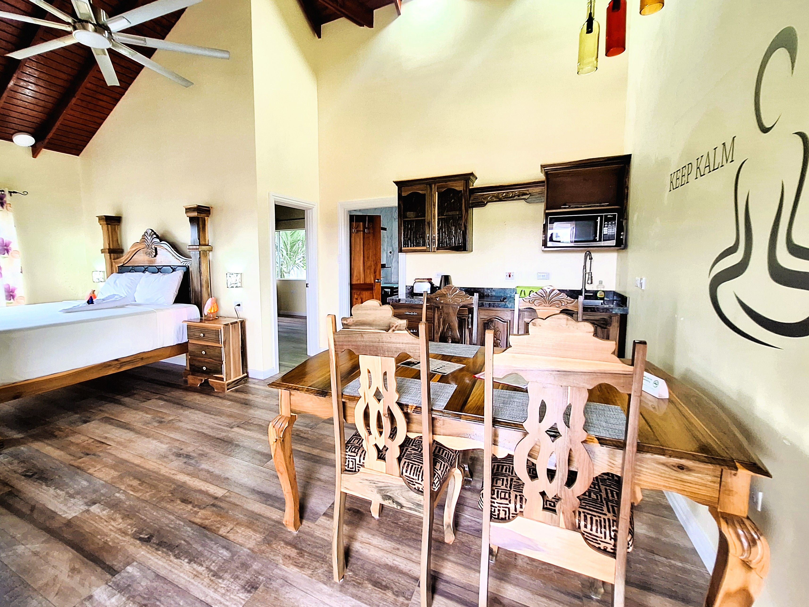 Una habitación amplia con cama, una mesa de comedor de madera, sillas y una cocina con microondas.