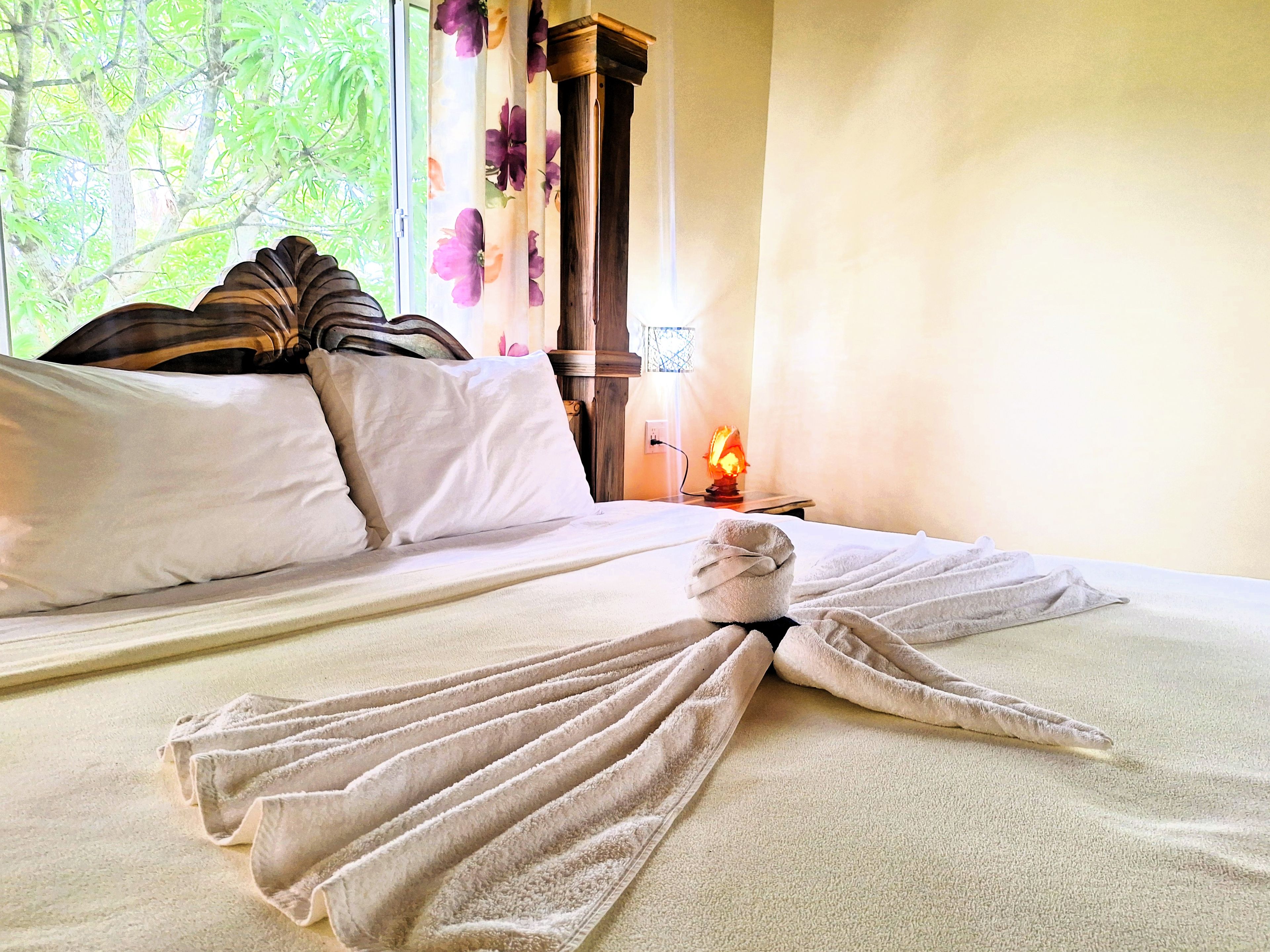 A neatly made bed with a folded towel and a bedside lamp.