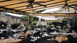 Un espacio exterior para comer con mesas, sillas, sombrillas y ventiladores de techo.