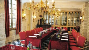 Un salón de banquetes con largas mesas, sillas rojas, candelabros y paredes de piedra.