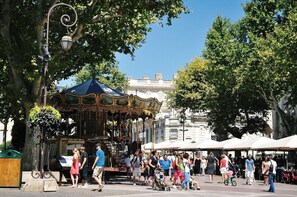 A carousel in a public square with people walking around. - Palais du Papes (Avignon)
