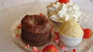 Un postre que incluye un pastel de chocolate, una bola de helado de vainilla y crema batida con una fresa encima.