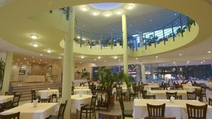 A multi-level restaurant with tables and chairs, a central column, and a view of the outside. - Bonita Beach Hotel (Golden Sands)