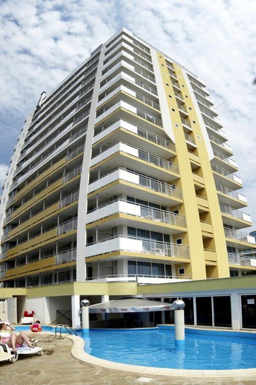 A multi-story hotel with balconies, a swimming pool, and a clear sky.