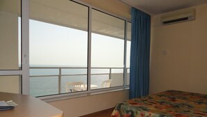 A hotel room with a large window, a bed with a colorful bedspread, a desk with a chair, and a view of the sea. - Bonita Beach Hotel (Golden Sands)