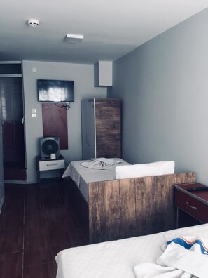 A hotel room with a bed, a wooden wardrobe, a small table with a fan, and a TV mounted on the wall. - Hotel Dinlen (Izmir)