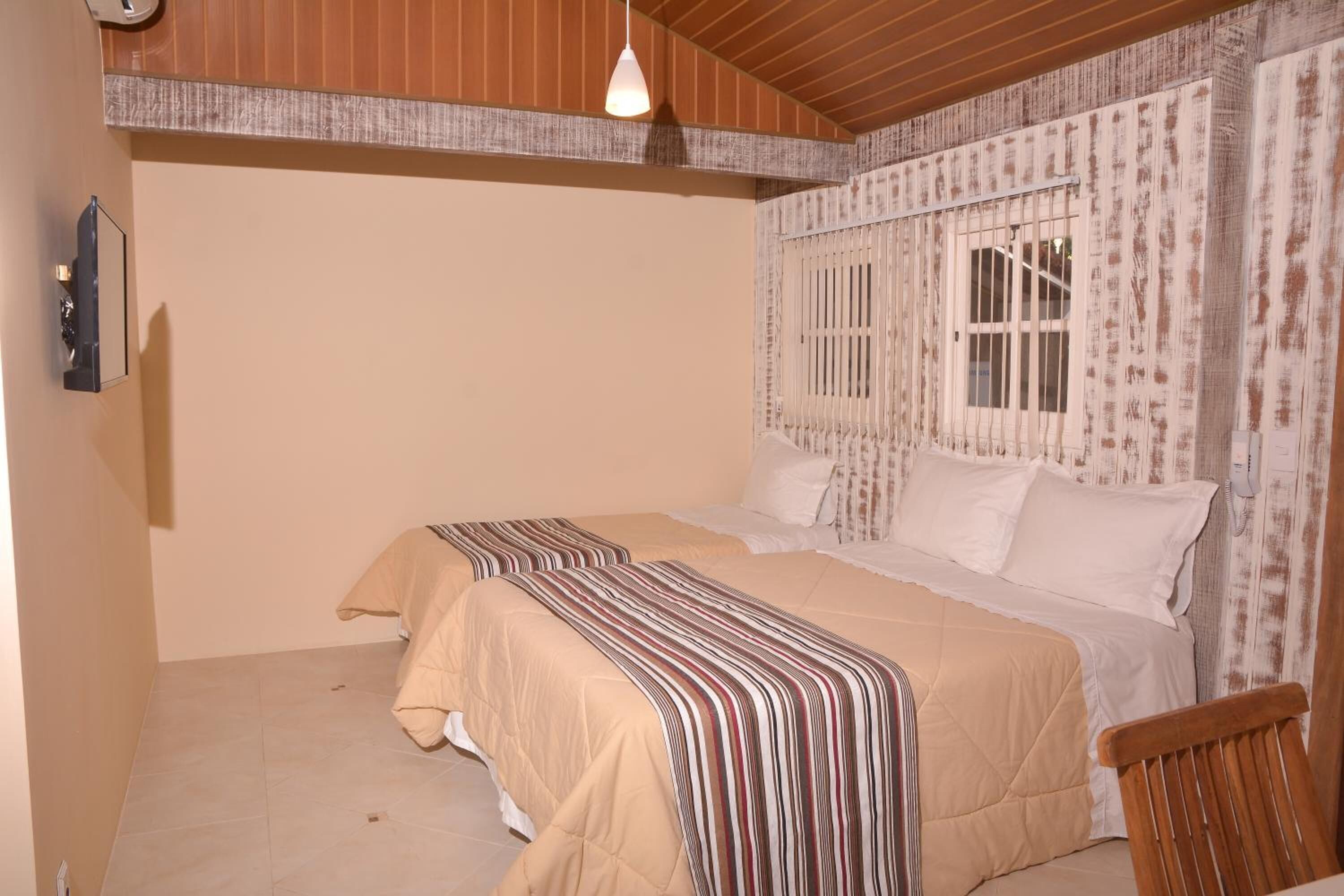 Une chambre avec deux lits, un plafond en bois, une fenêtre avec des barreaux et un téléphone fixé au mur.