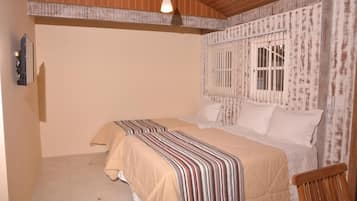 A bedroom with two beds, a wooden ceiling, a window with bars, and a wall-mounted phone.
