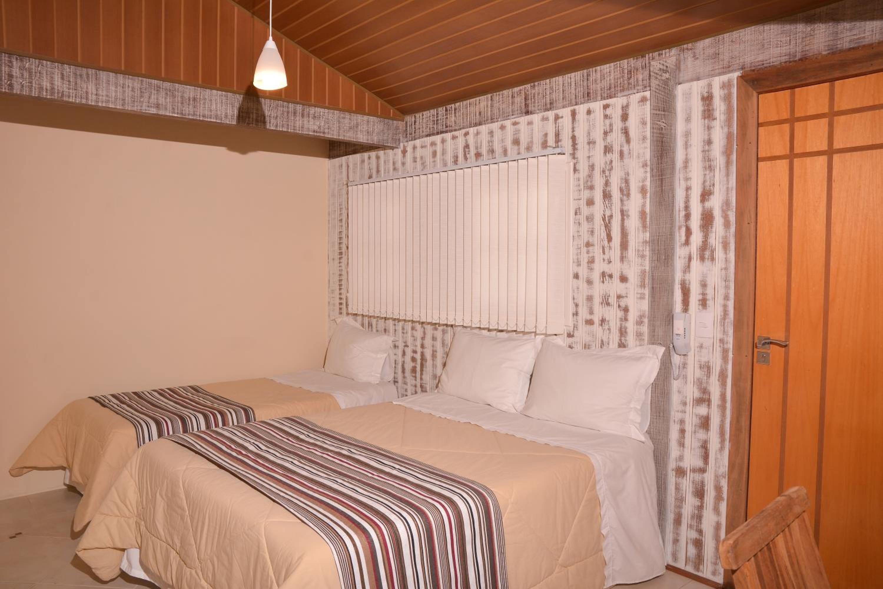 A bedroom with two beds, wooden ceiling beams, a striped bedspread, and a wooden door.