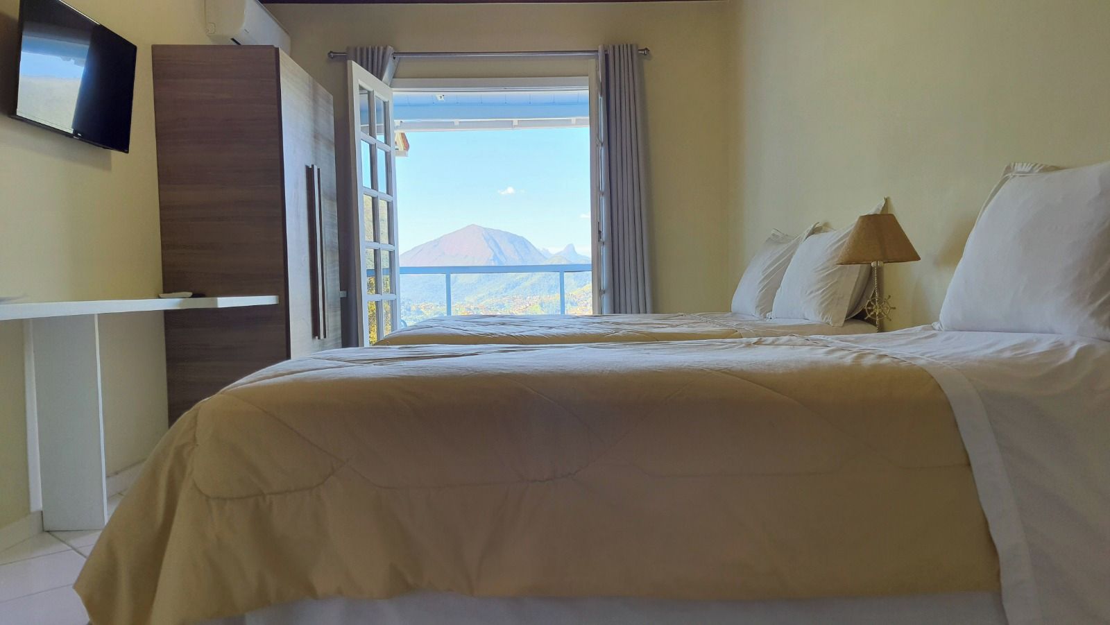 A hotel room with a bed, a television, a window with curtains, and a view of a mountain.