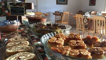 A buffet with various desserts, including cakes and pastries, in a dining area with wooden chairs and a checkered tablecloth.