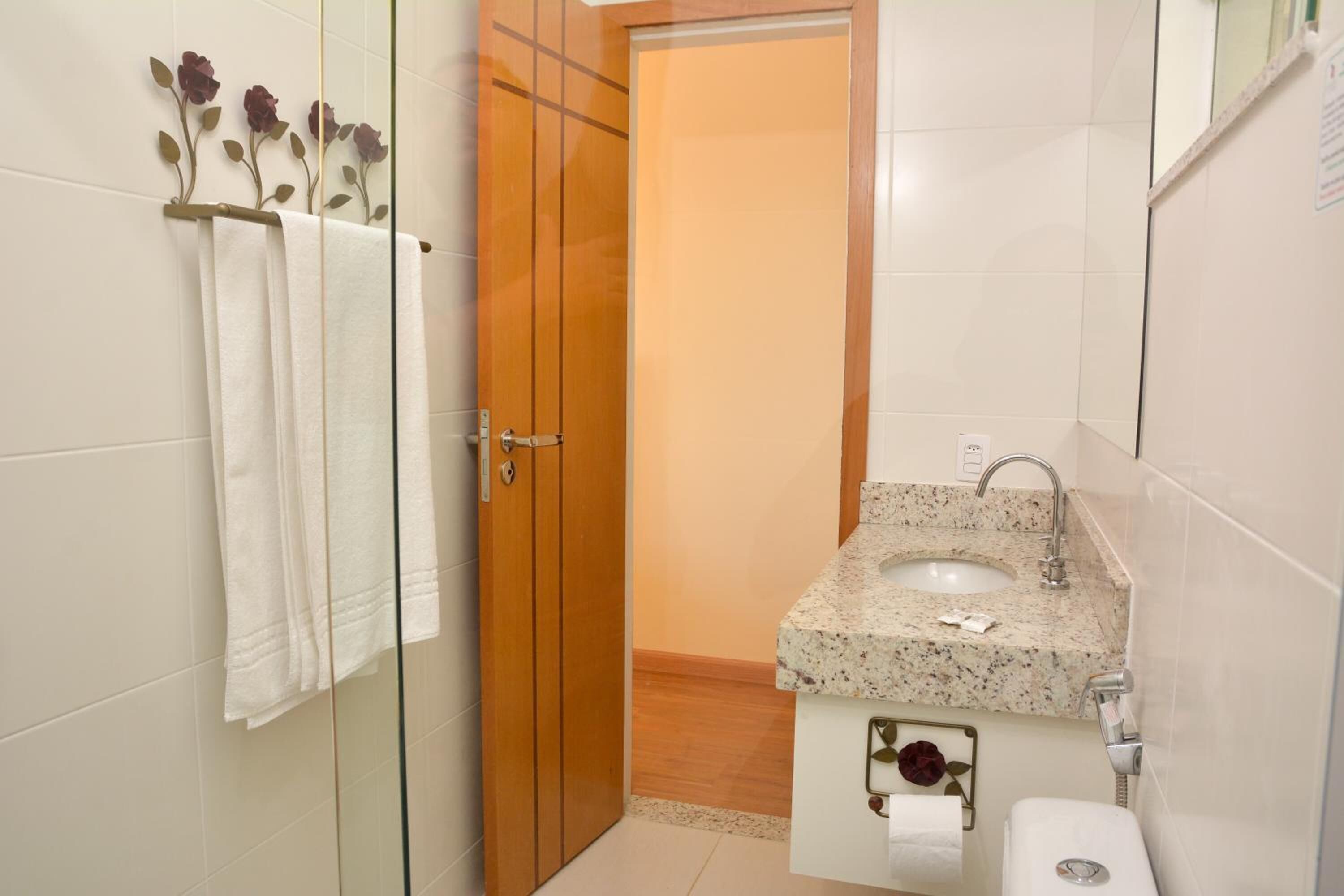 A bathroom with a wooden door, a sink with a marble countertop, and a glass shower enclosure.