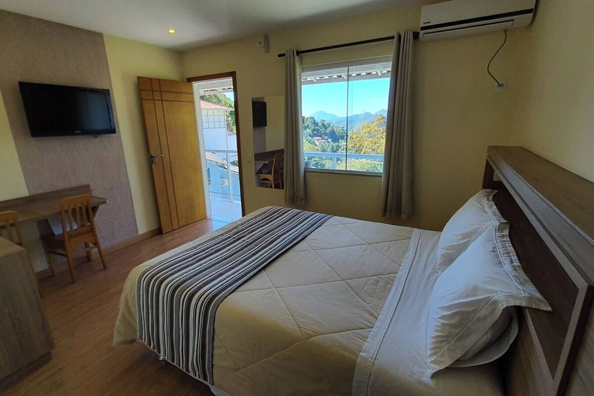A hotel room with a bed, a desk, a TV, and a window with a view of the outdoors.