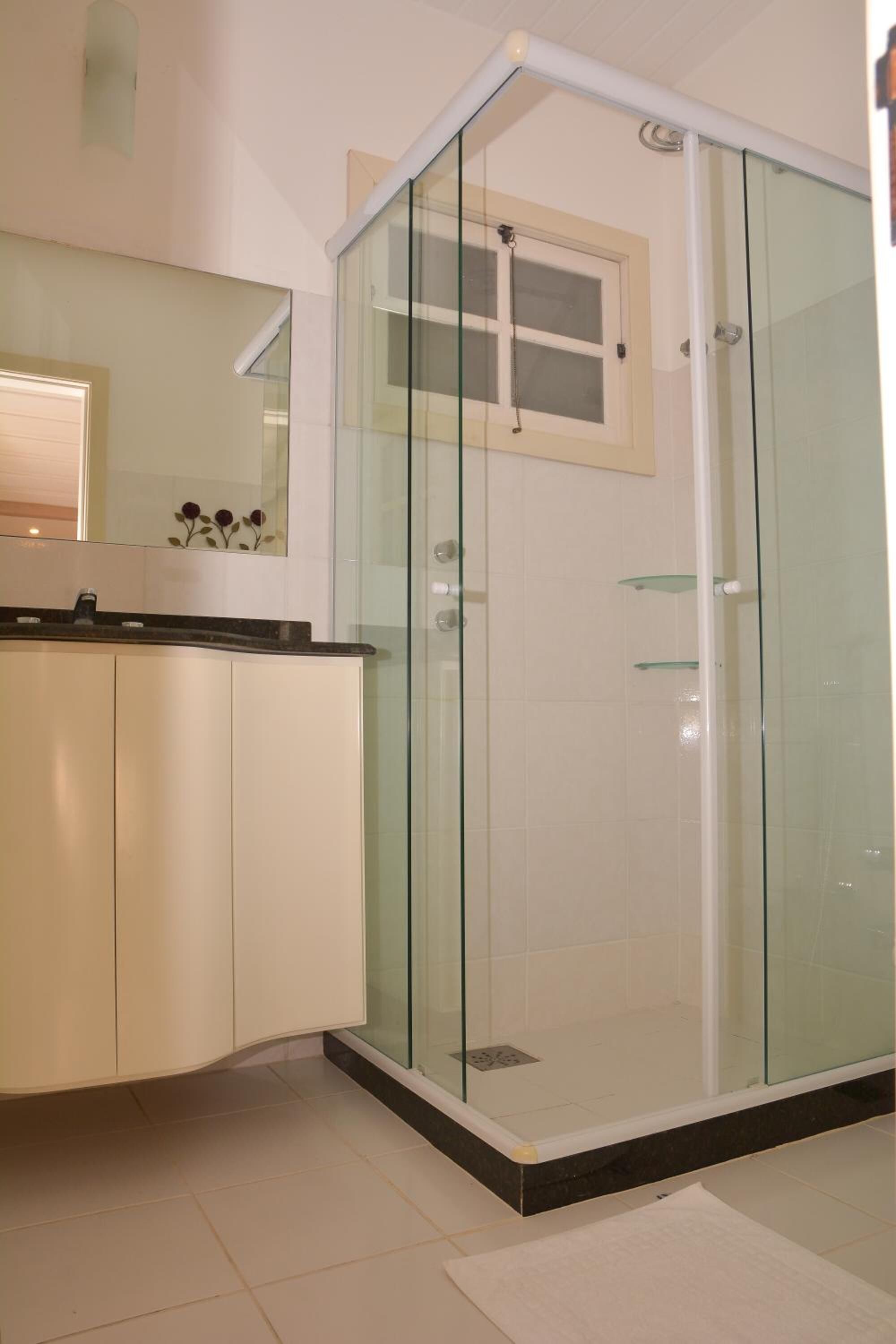 A modern bathroom with a glass shower enclosure, a white tiled floor, and a countertop with a sink.