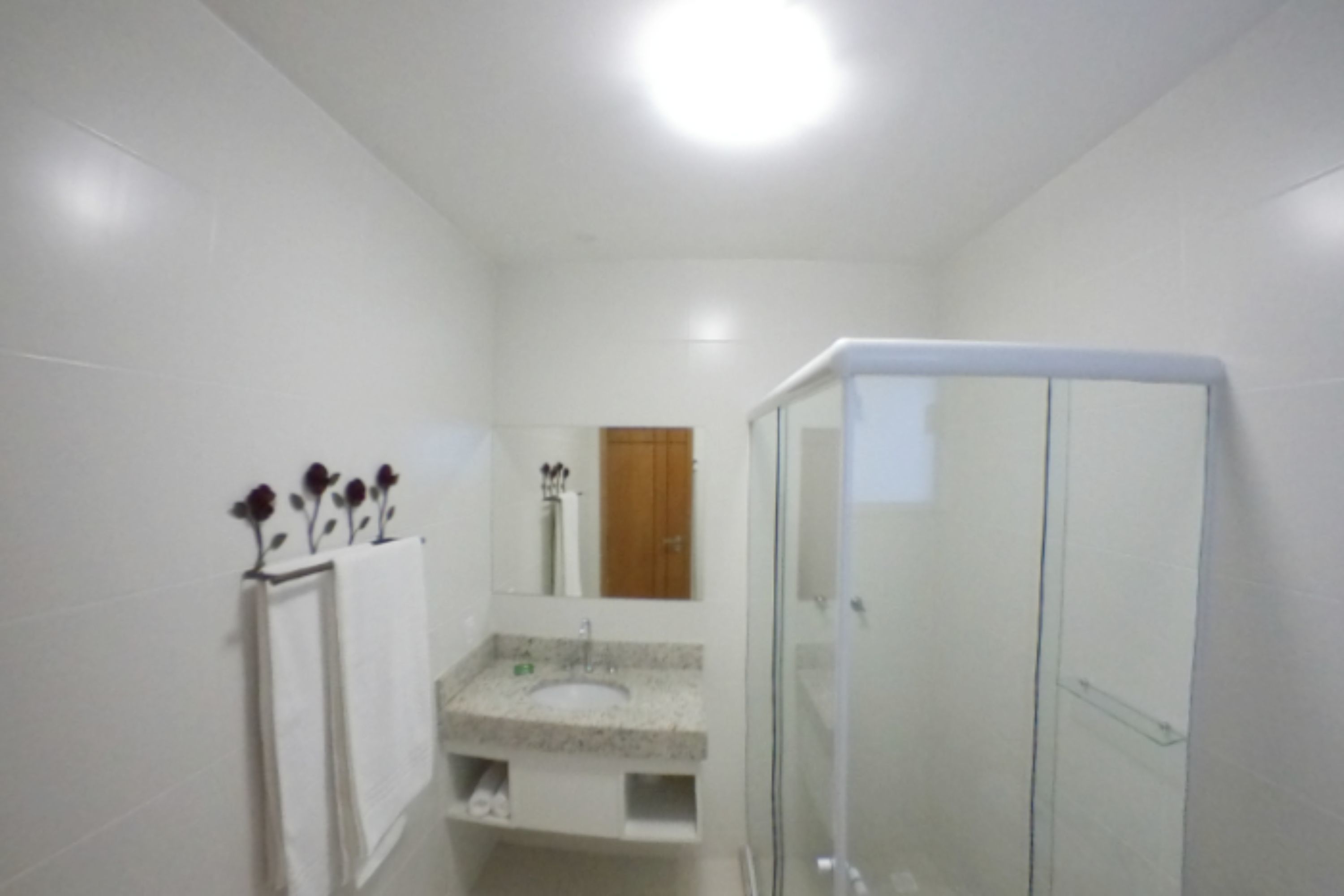 Un baño con ducha de vidrio, lavamanos con encimera de mármol y espejo sobre el lavamanos.