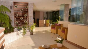 Un vestíbul ampli amb una taula de recepció, mobles de vimet i plantes en testos.