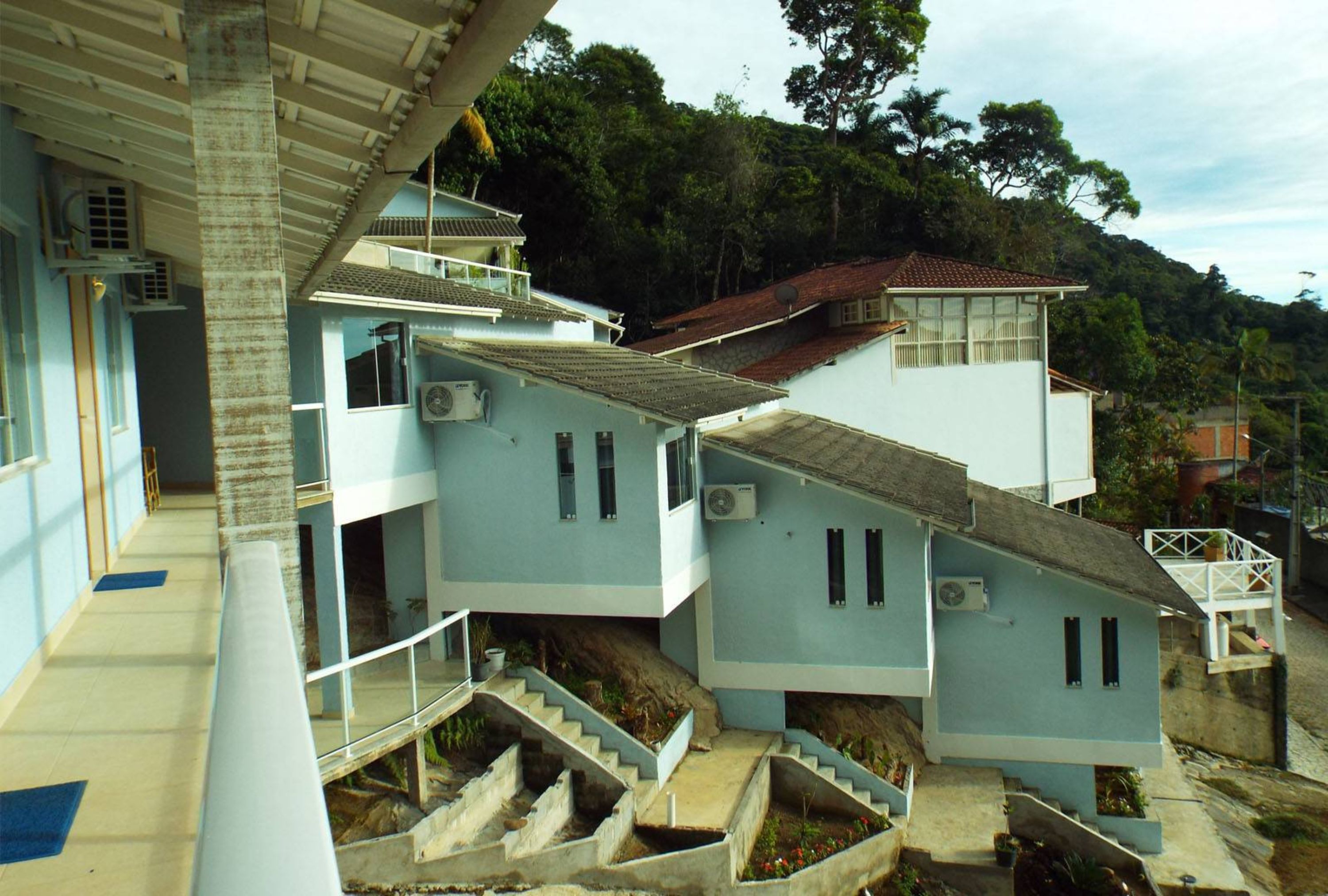 Un edificio de varios pisos con una escalera que lleva a un balcón, rodeado de follaje y árboles.