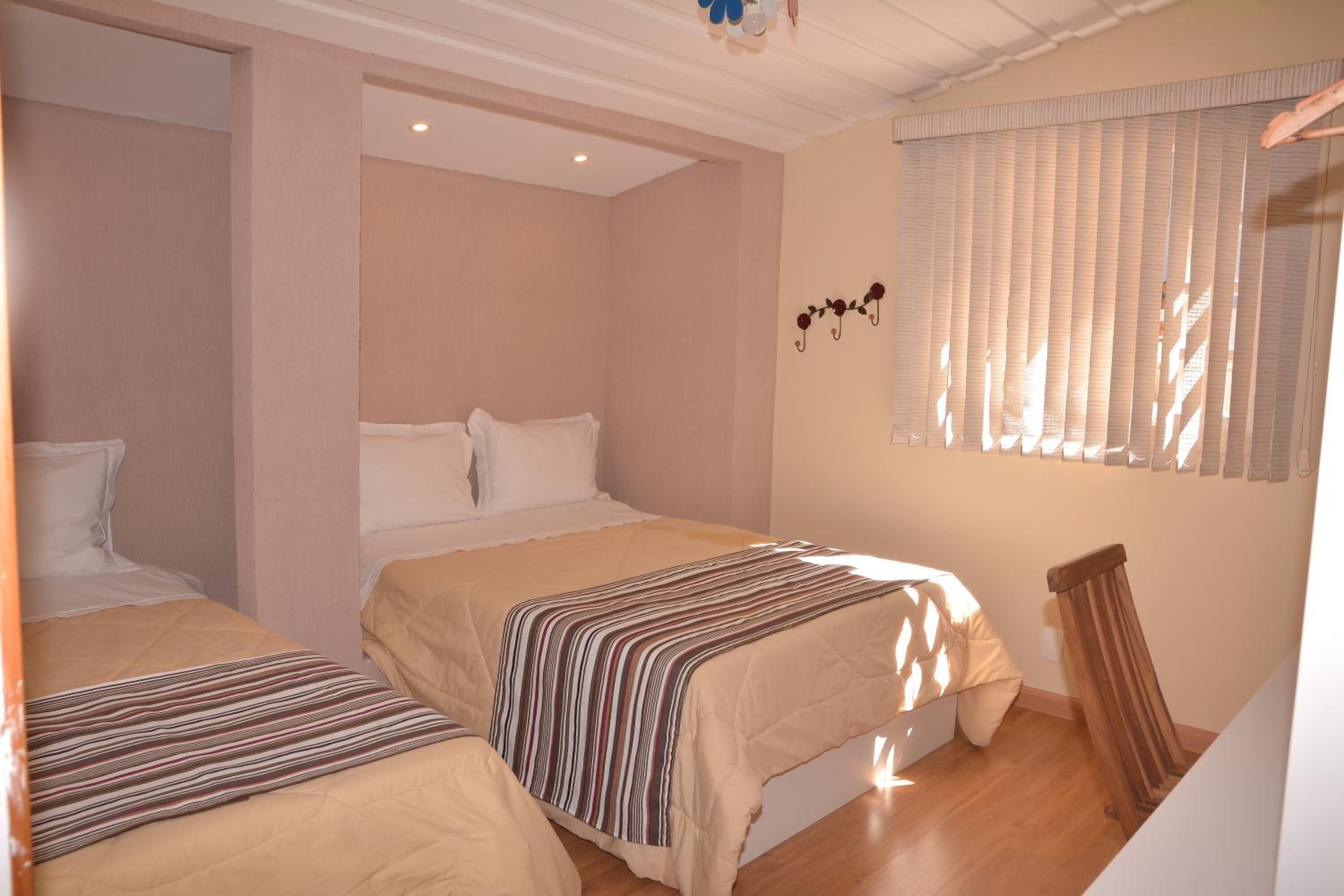 A bedroom with two beds, a wooden floor, and a window with blinds.