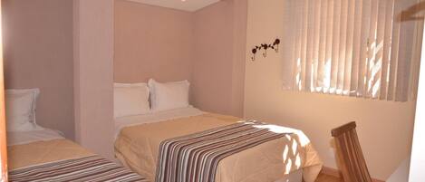 A bedroom with two beds, a wooden floor, and a window with blinds.
