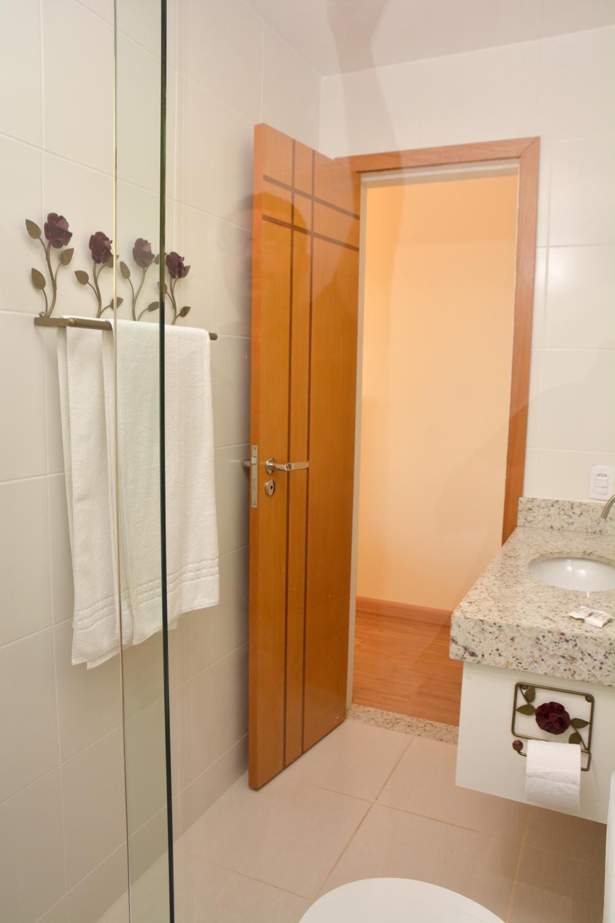 Uma casa de banho com cabine de duche em vidro, porta de madeira, lavatório com bancada de mármore e sanita.