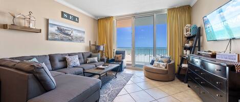 A living room with a sofa, armchair, TV, and a balcony with a view.