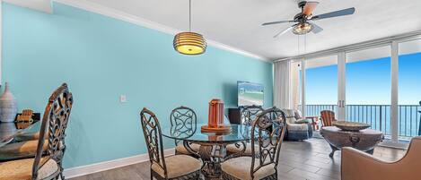 A dining area with a glass table, ornate chairs, a ceiling fan, and a view of the ocean.