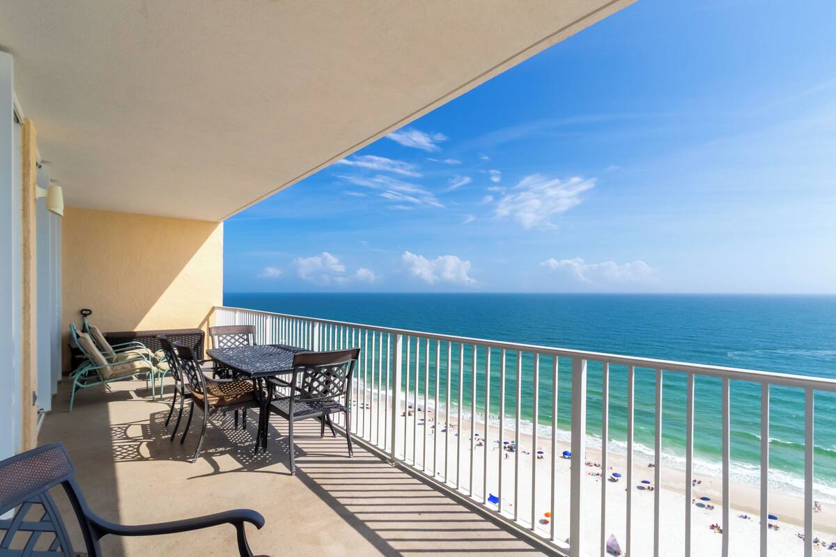 Un balcon avec vue sur l’océan et la plage, aménagé avec des chaises et une table.