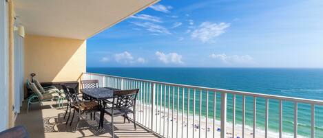 Varanda com vista para o oceano e a praia, mobiliada com cadeiras e uma mesa.