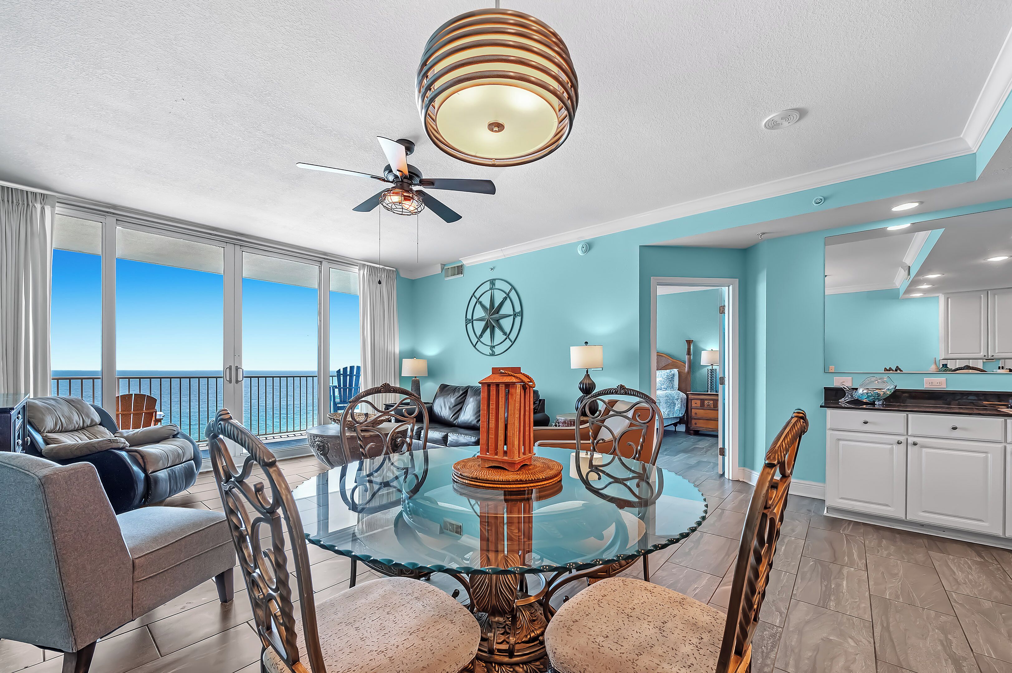 A spacious living area with a glass dining table, a ceiling fan, and a view of the ocean.