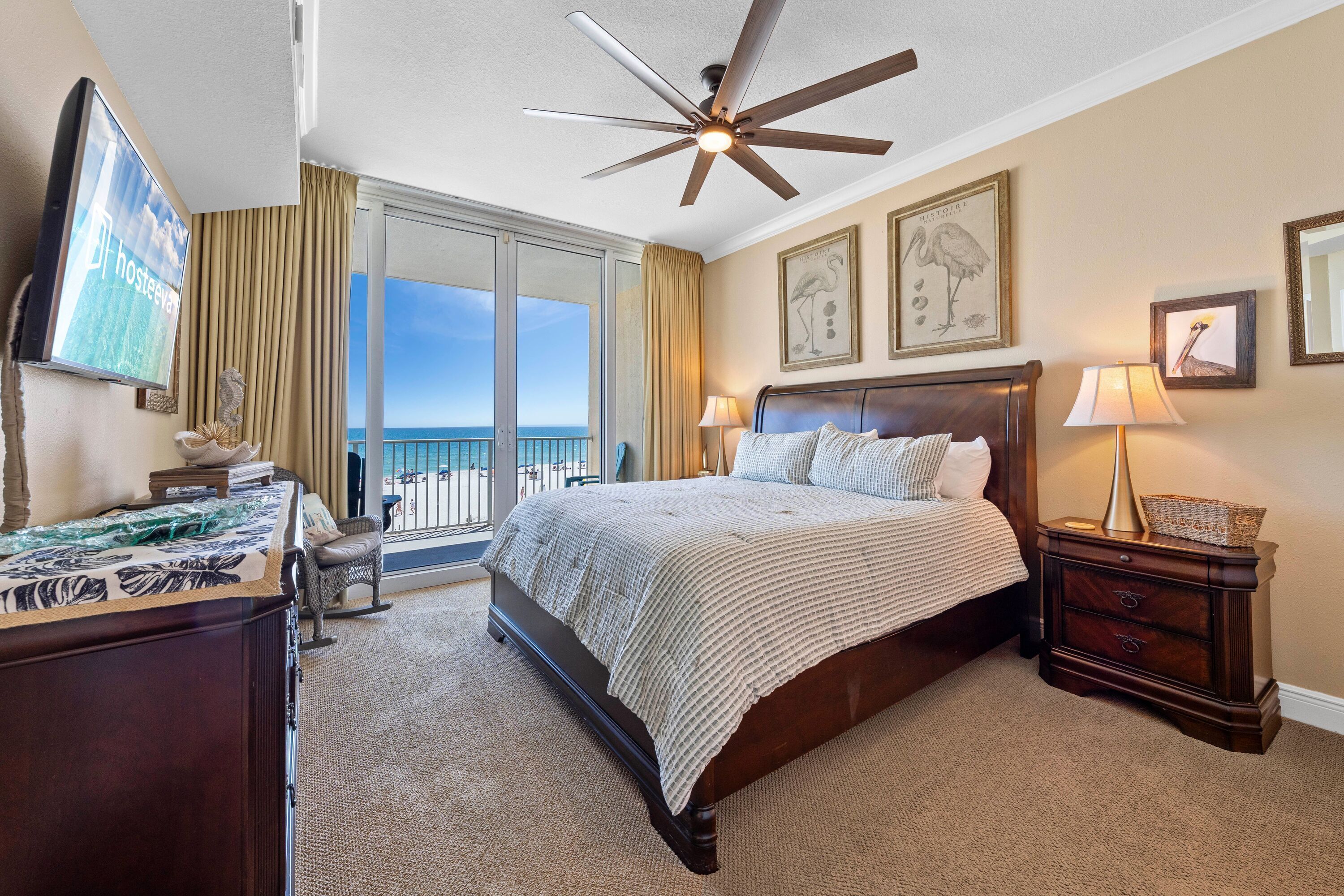 A hotel room with a bed, a desk, a chair, a ceiling fan, a TV, and a balcony with a view.