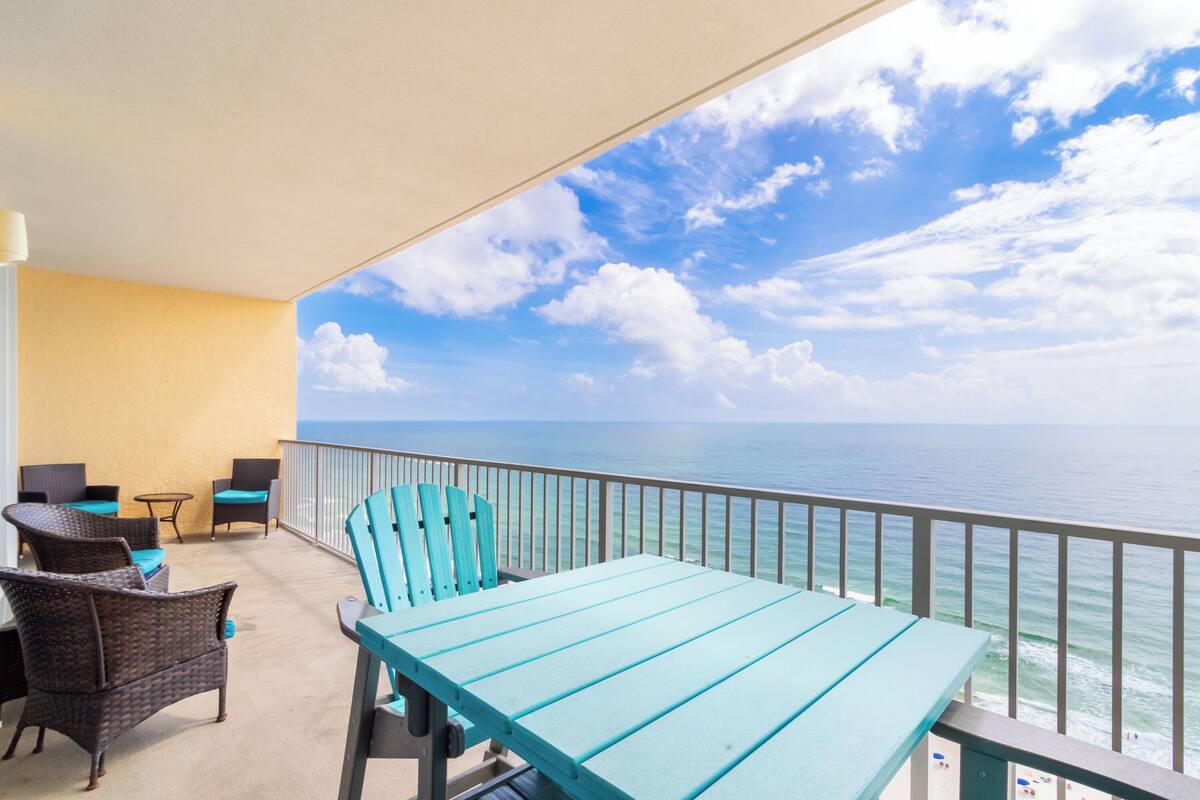 Un balcon agrémenté de meubles en osier, d’une table turquoise et offrant une vue sur l’océan.