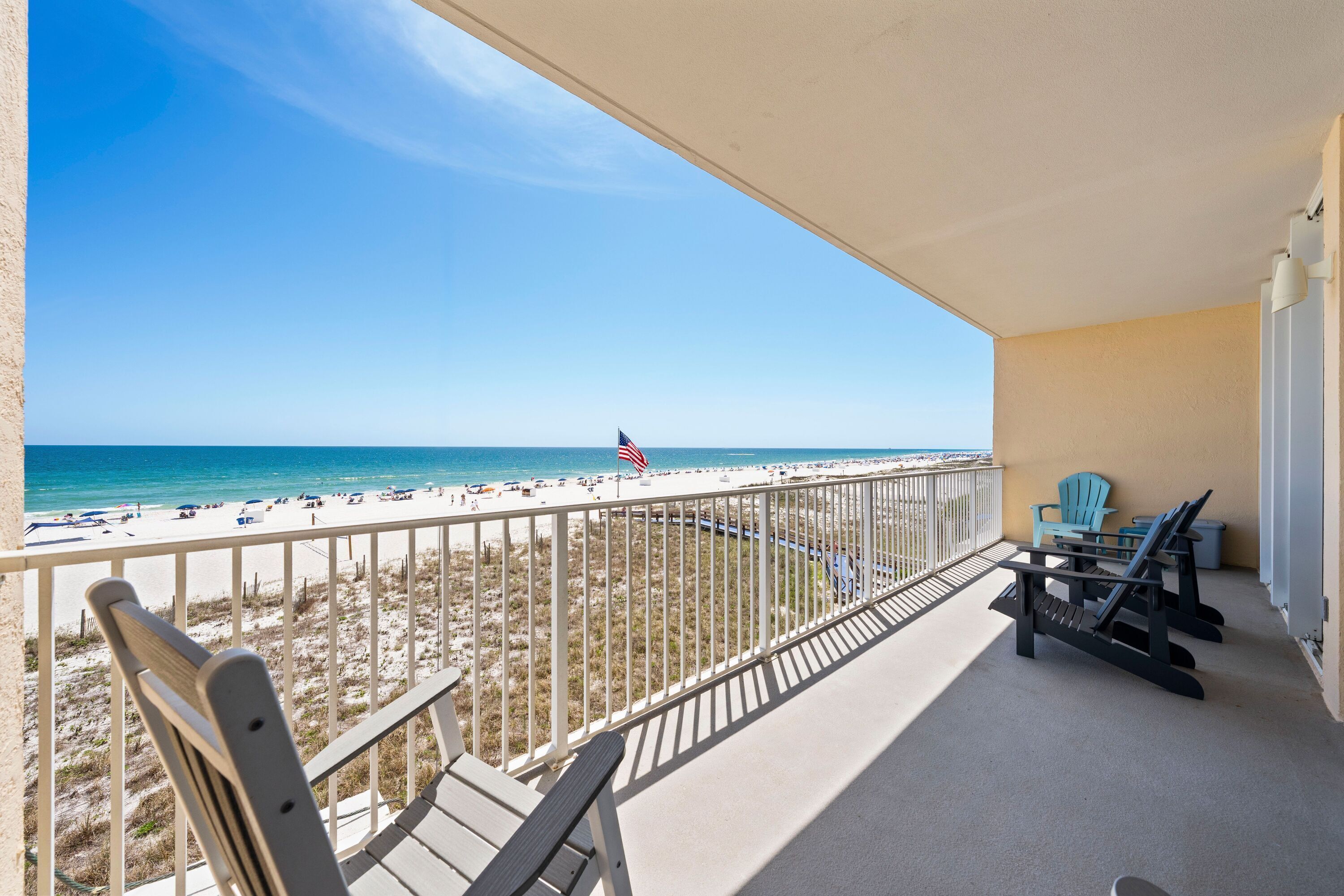 A balcony with a view of the beach, a flag, and outdoor furniture.