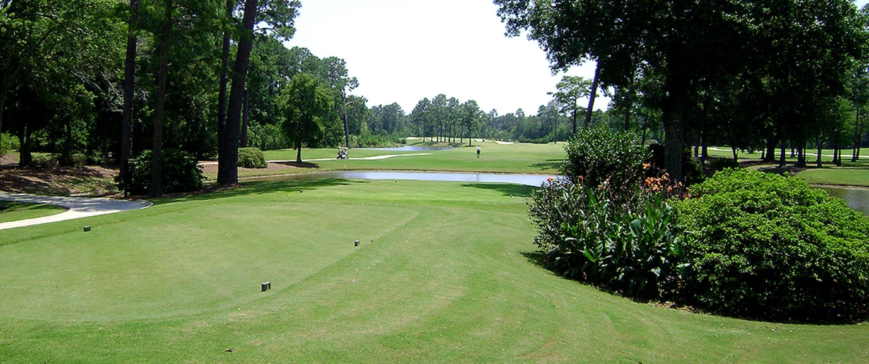 Un campo de golf con un estanque, árboles y césped bien cuidado.