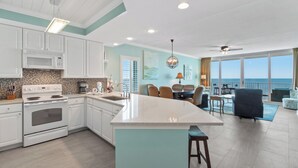 A modern kitchen with white cabinets, a large island, and a view of the ocean. - San Carlos Condos (Gulf Shores)