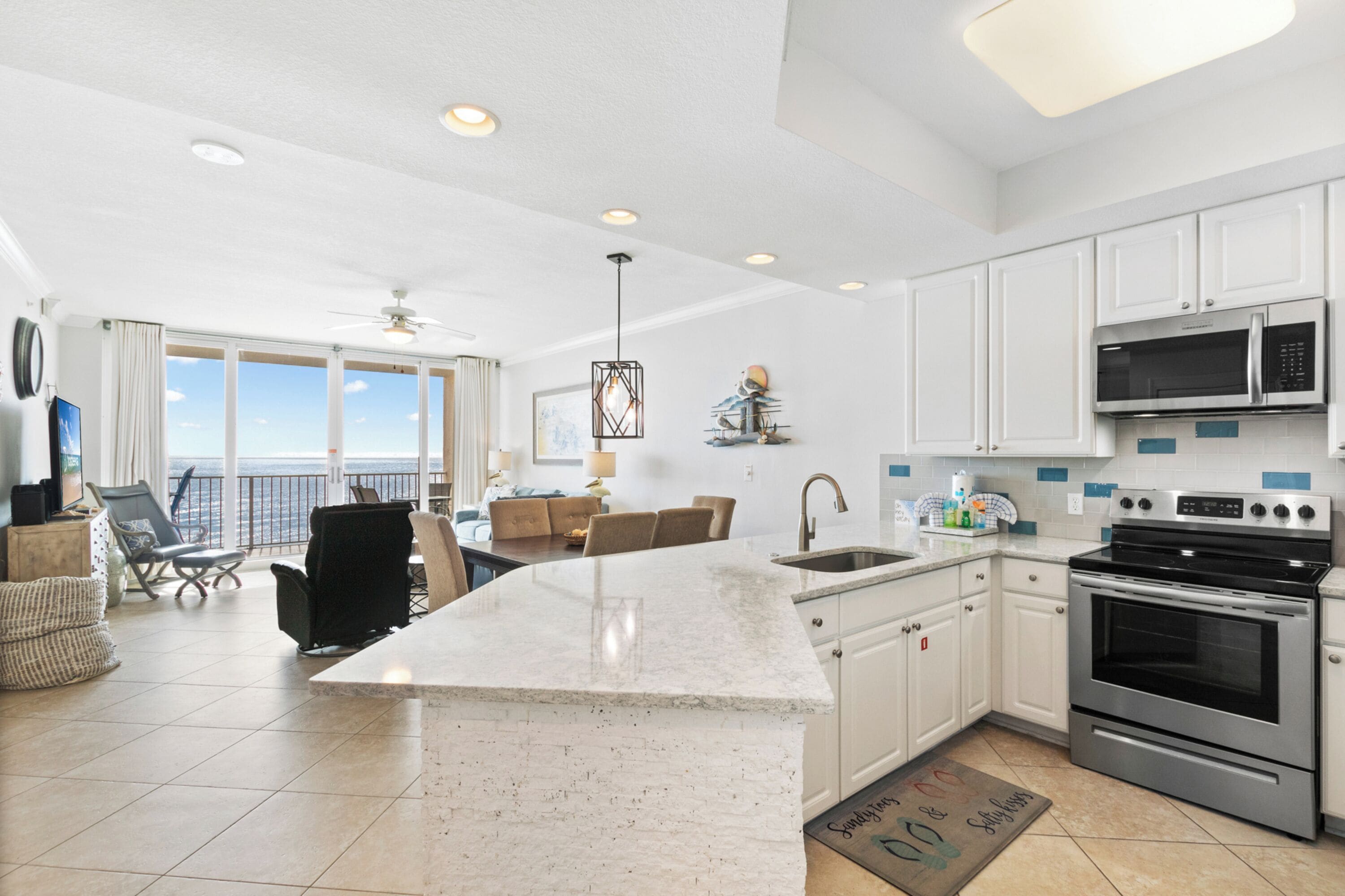 A modern kitchen with white cabinets, a large island, stainless steel appliances, and a view to the outside.
